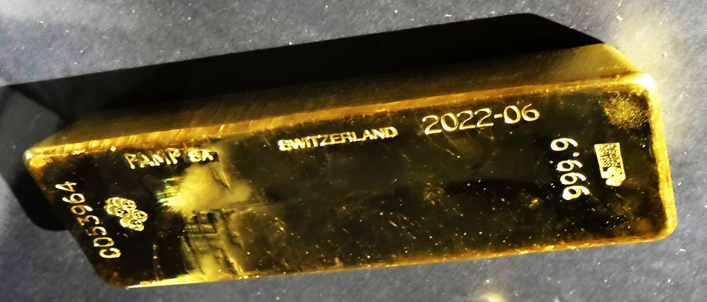 A cast gold bar seen from above at an angle, stamped PAMP SA, SWITZERLAND, 2022-06, 999.9 and the serial number C053964, with the refiner's logo beside the serial