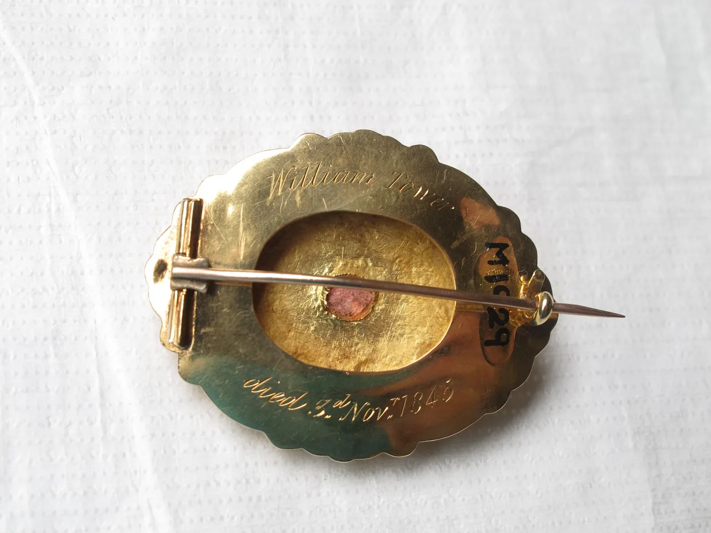 Back of a gold memorial brooch engraved William Tower, died 3rd Nov 1845, showing a tube hinge on the left, a pin stem running across the back, and its point projecting past a plain C-catch on the right
