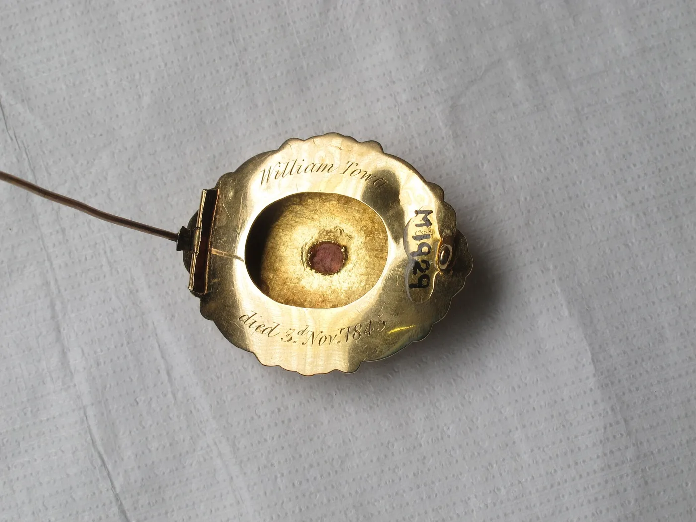 The same memorial brooch with its pin swung fully open, so the tube hinge stands clear of the back plate and the glazed compartment at the centre is visible
