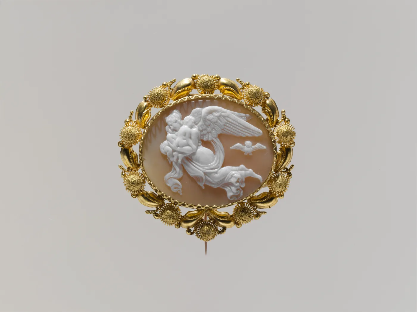 Shell cameo pin carved in relief with a classical scene, framed by a chased gold border of leaves