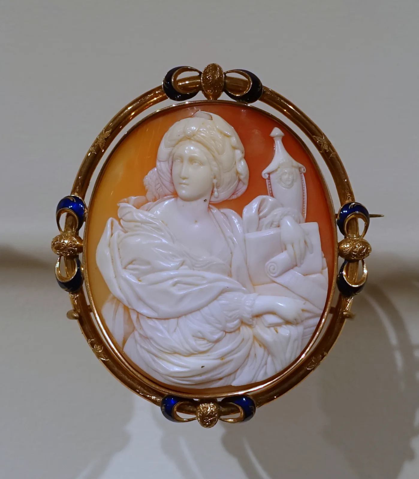 Shell cameo brooch carved with a woman's profile in white relief against the warm brown underlayer of the shell, set in a plain gold bezel