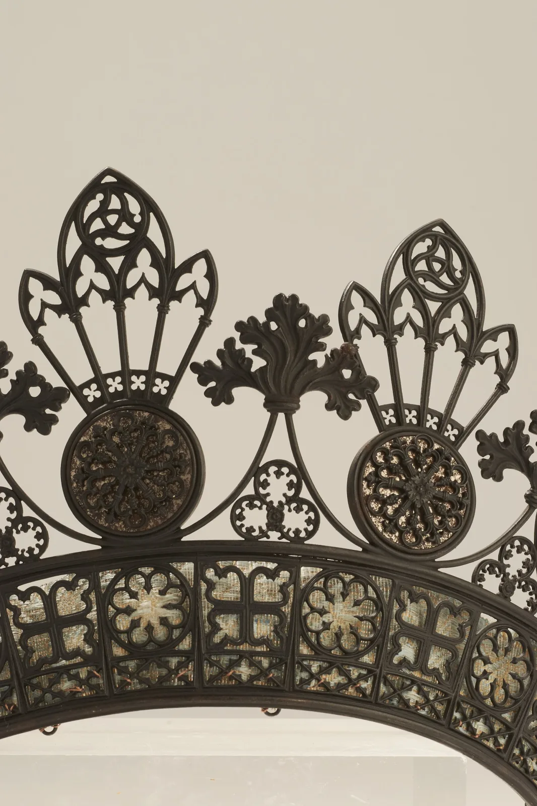 Close view of a cast iron tiara showing pointed-arch tracery, trefoil and quatrefoil piercings, rosette roundels and sprays of oak leaves, all rendered in crisp openwork