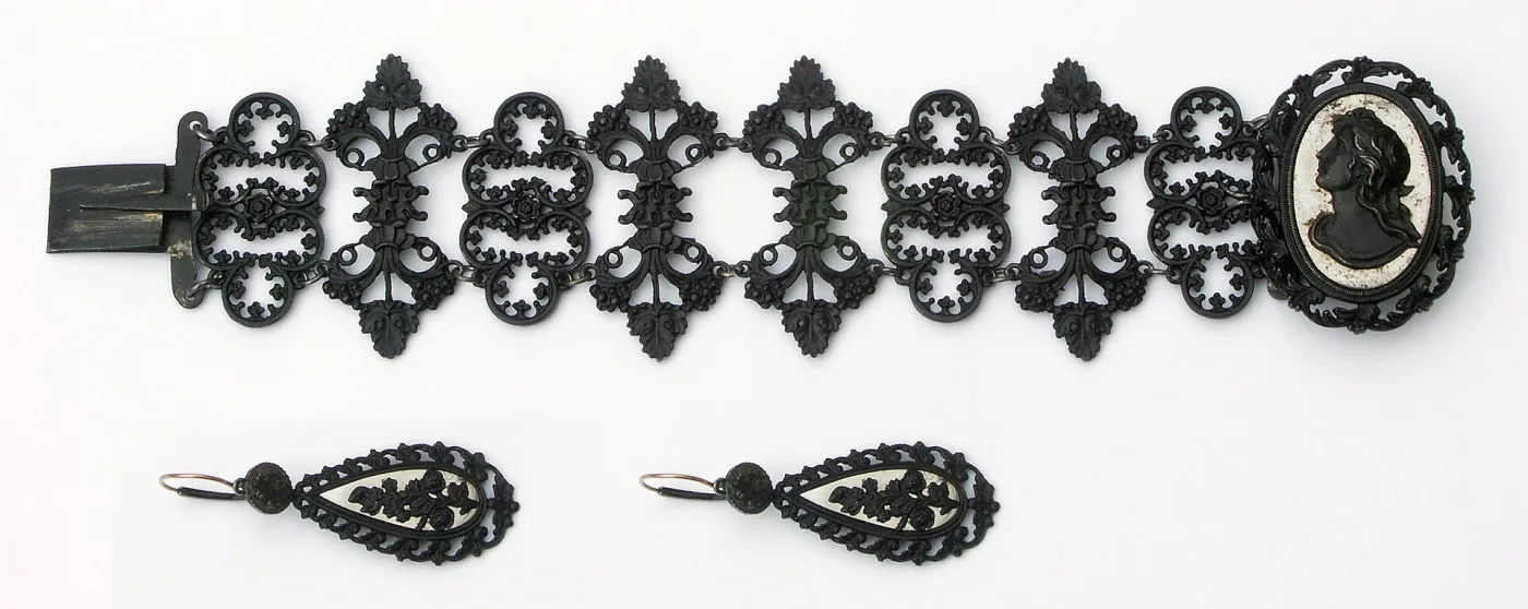 Berlin iron bracelet of pierced scroll links with a clasp medallion showing a black profile head against a white ground, with two matching pierced drop earrings below