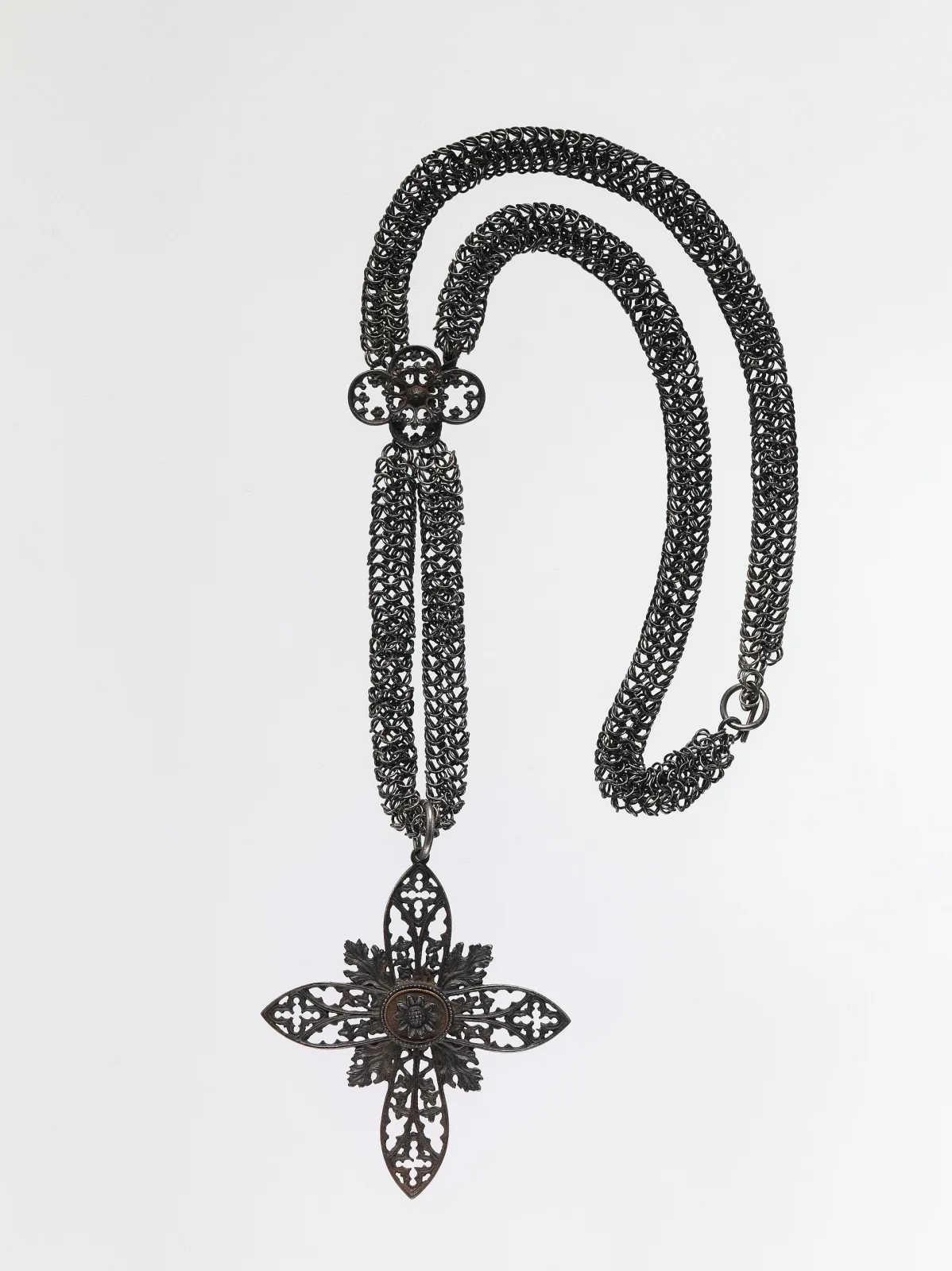 Long iron chain of fine wire mesh links passing through a quatrefoil slide, ending in a pierced cross pendant with Gothic tracery in each arm and a rosette boss at the centre