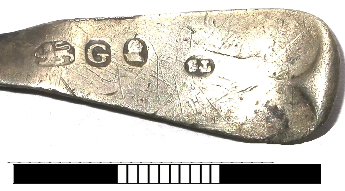 Close-up of four marks struck along a silver spoon handle: a maker's mark, a walking lion, a leopard's head and a date letter, with a scale bar beneath