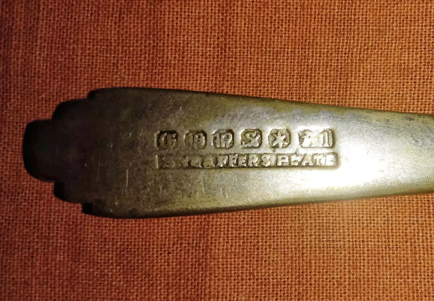 Row of six small struck marks on a spoon handle imitating a hallmark sequence, with the words SHEFFIELD PLATE stamped in a rectangle directly beneath them