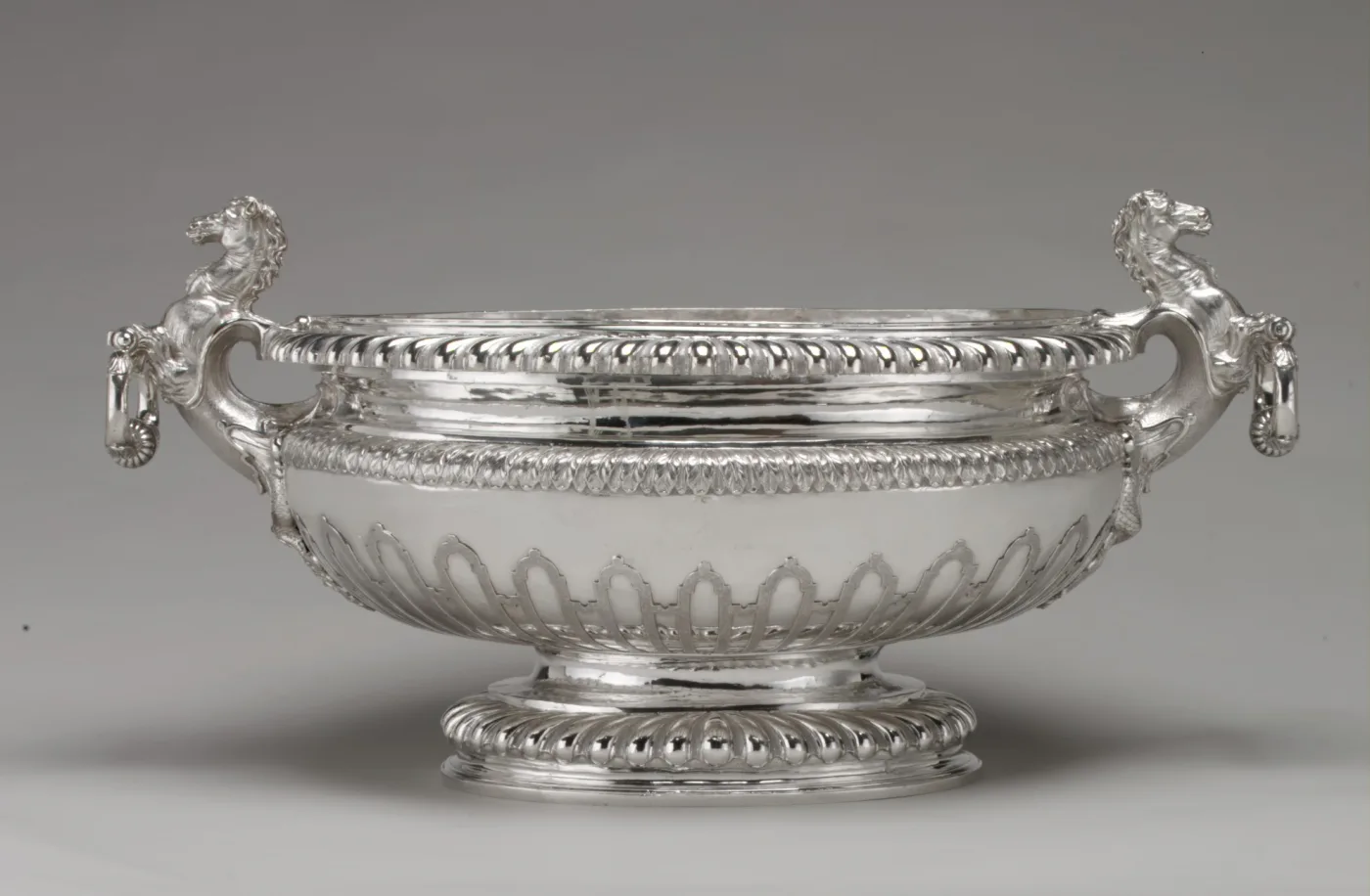 Large oval silver wine cistern with lion mask handles and a gadrooned rim, standing on a moulded foot