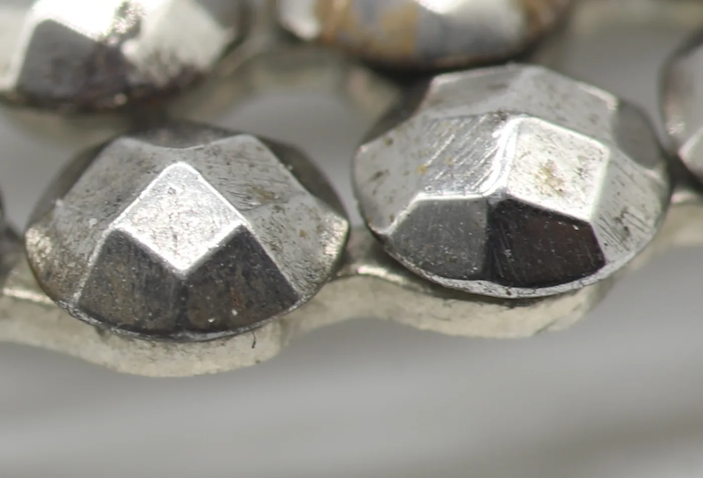 Extreme close-up of two steel studs showing a flat five-sided table facet on top with angled facets falling away around it, mounted on a shared metal strip
