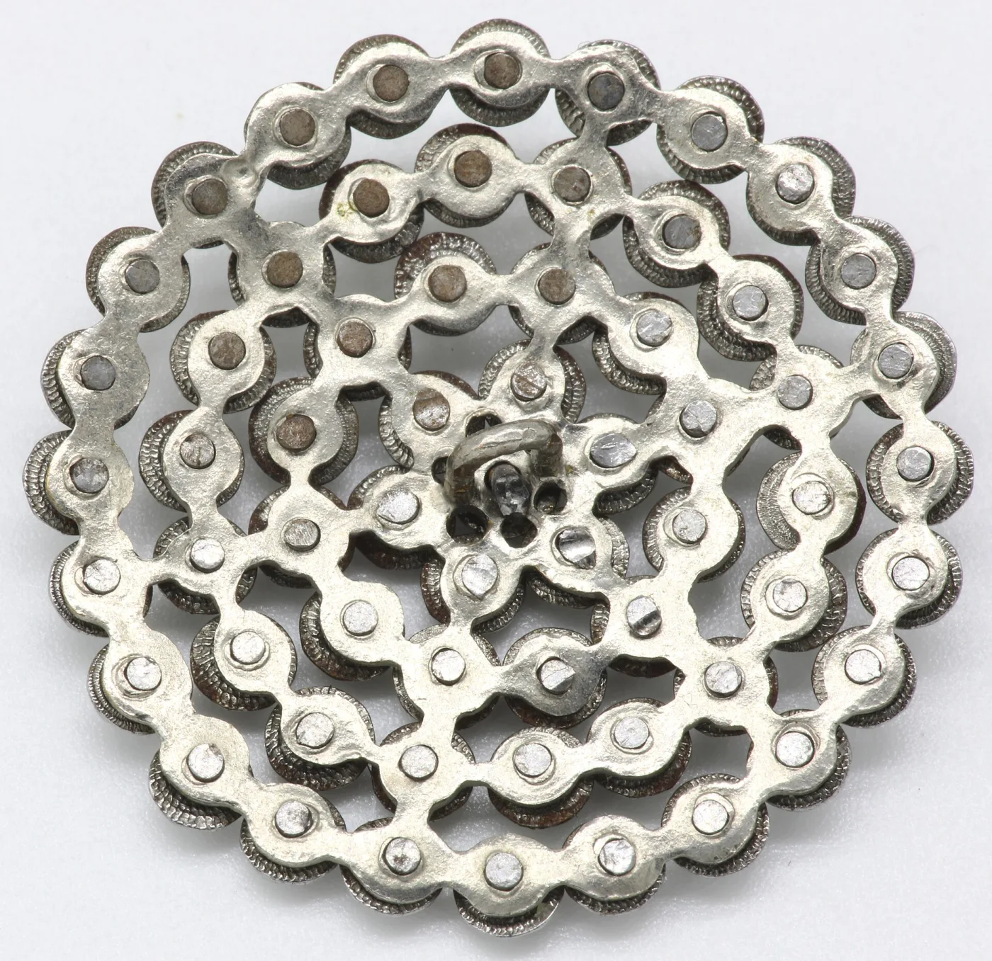 Reverse of a pierced steel rosette button showing a flattened rivet tail behind every stud position across the openwork plate