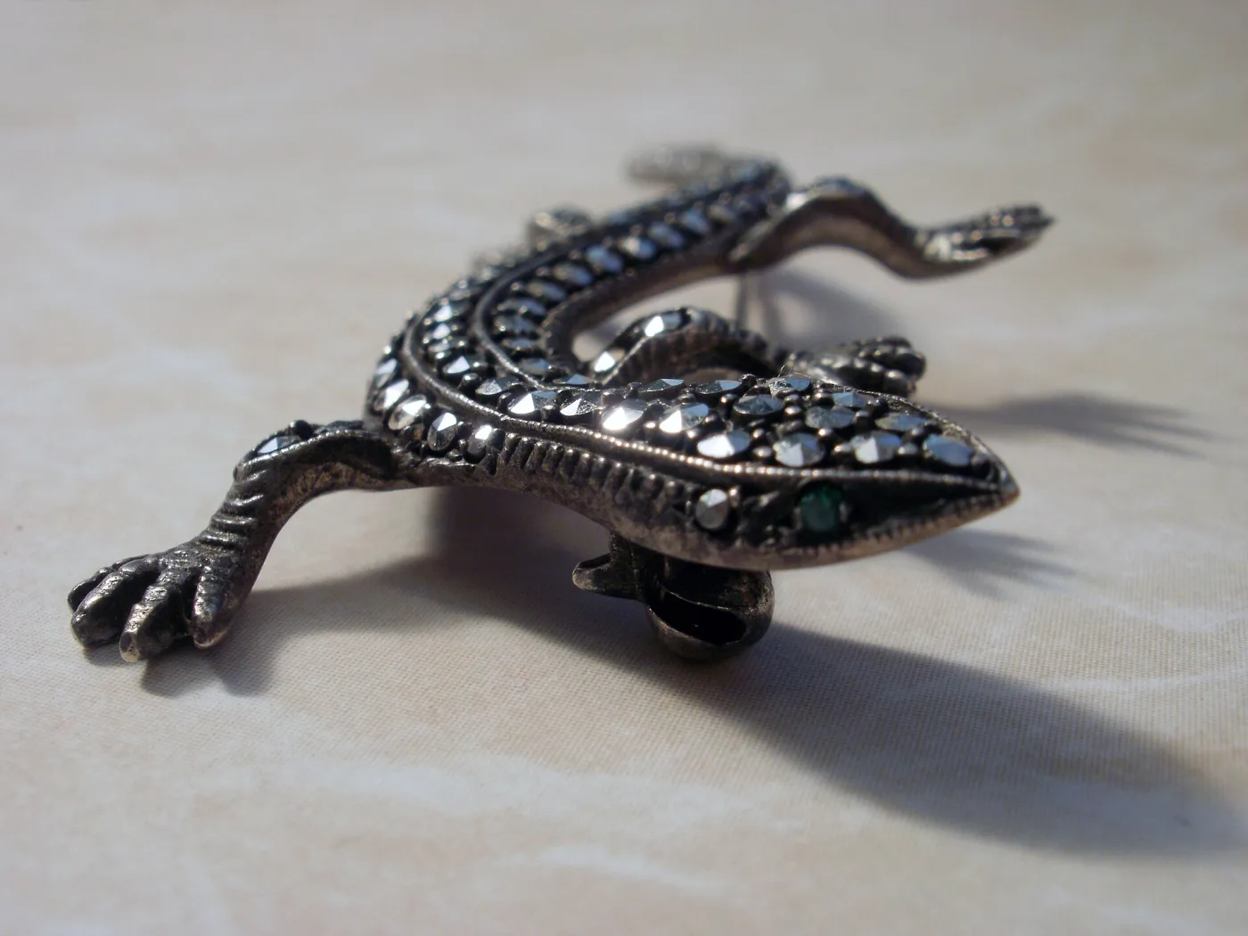 Close view of a silver lizard brooch densely set with small dark pyrite stones of visibly varying size, with a green stone for the eye