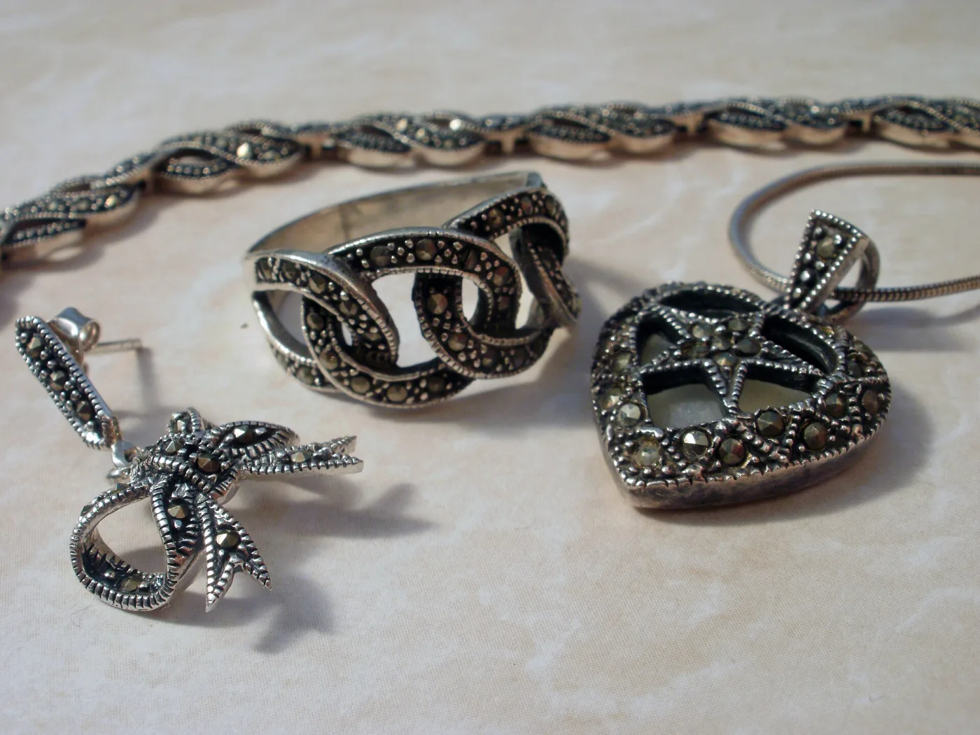 Group of silver marcasite pieces including a link bracelet, a wide ring, a bow-shaped drop earring and a heart-shaped pendant, all pave set with small pyrite stones