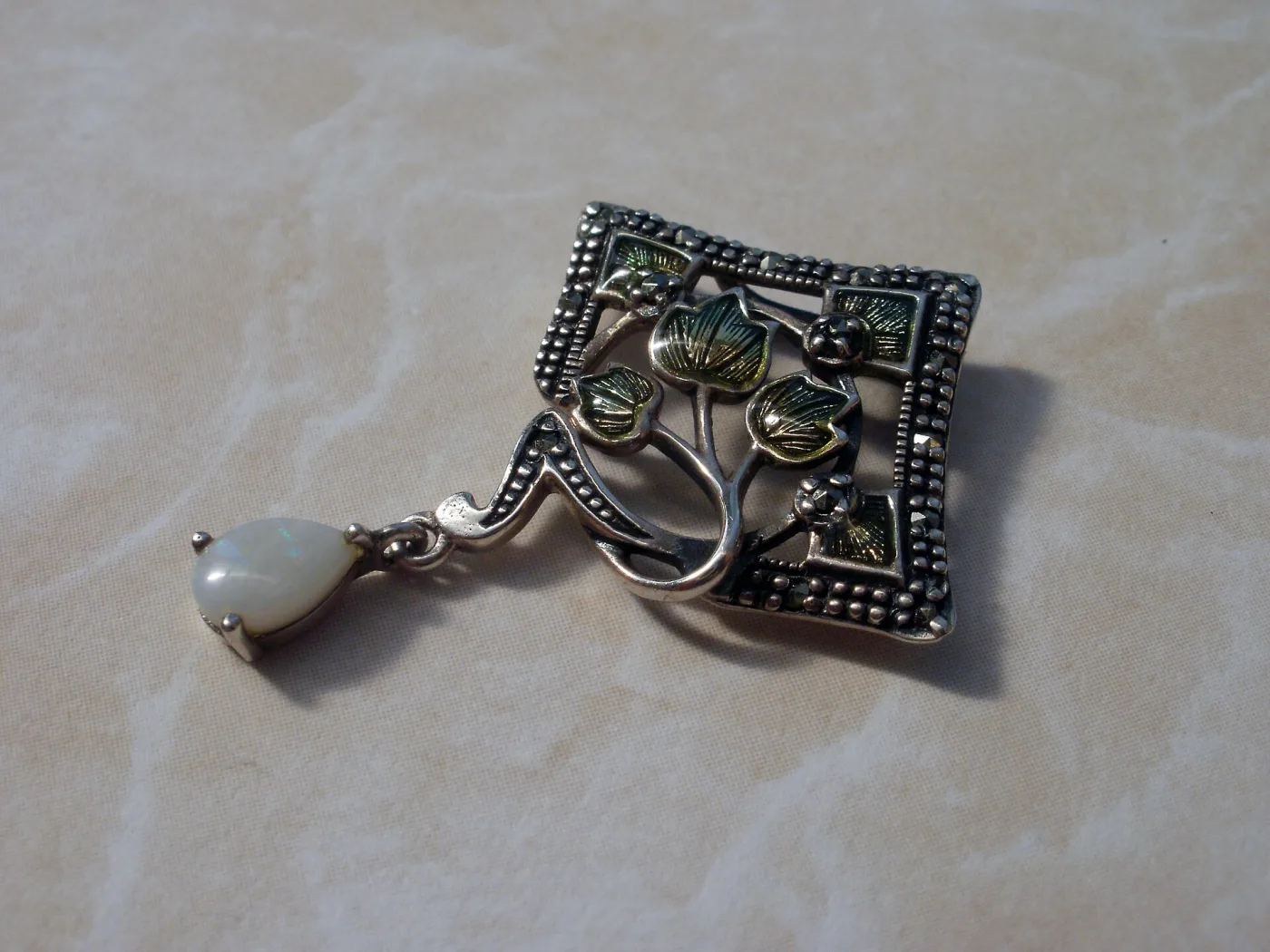 Silver pendant set with small pyrite stones around a pale opal cabochon, with an opal briolette drop hanging beneath
