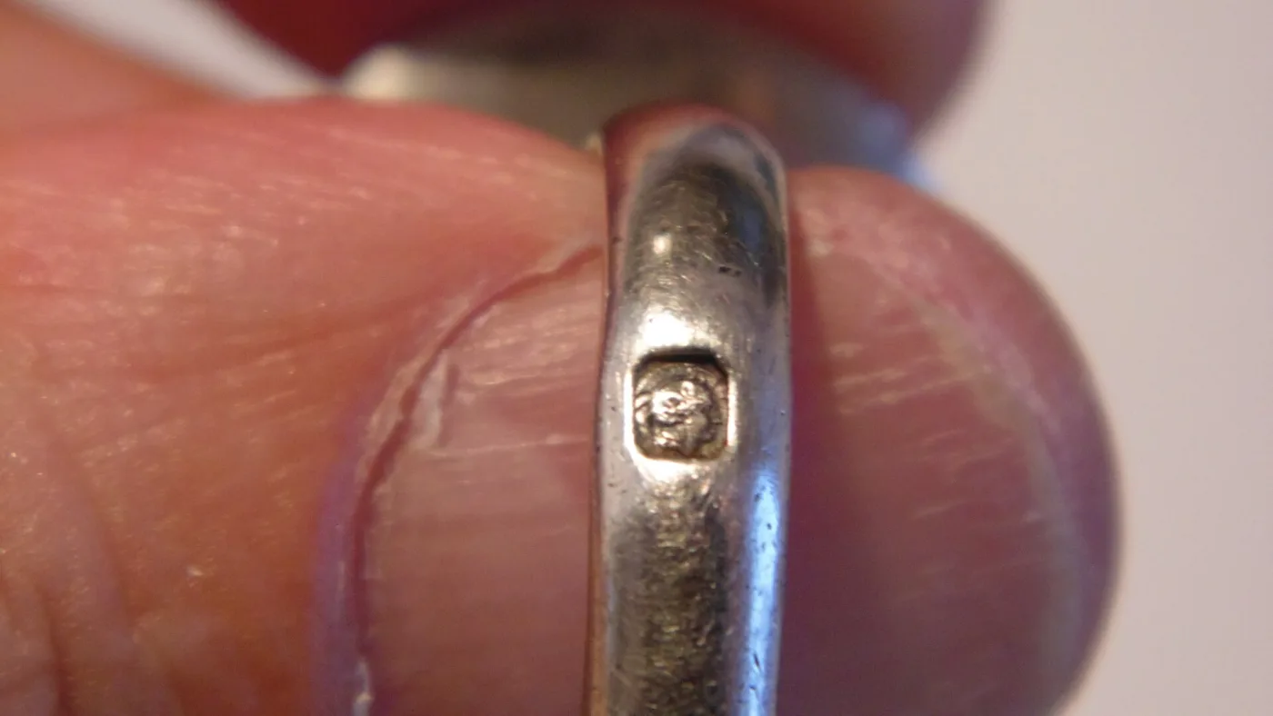 A ring band held between finger and thumb, a single small oval punch struck into the outer surface of the shank