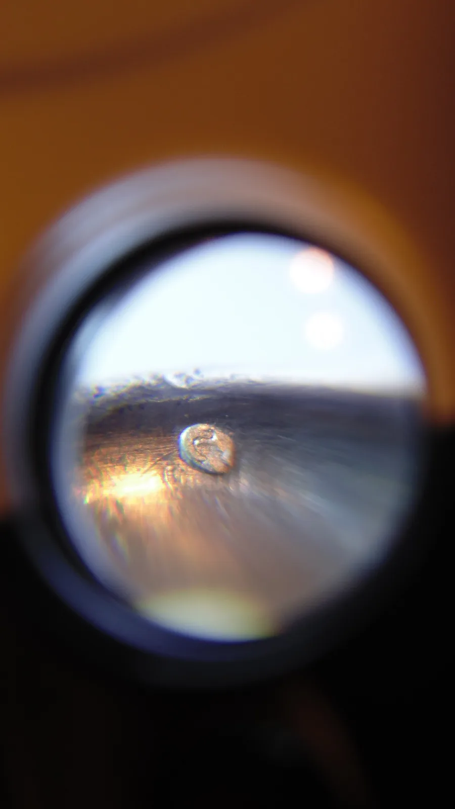 A jeweller's loupe held over a metal surface, the small struck punch visible and magnified inside the lens