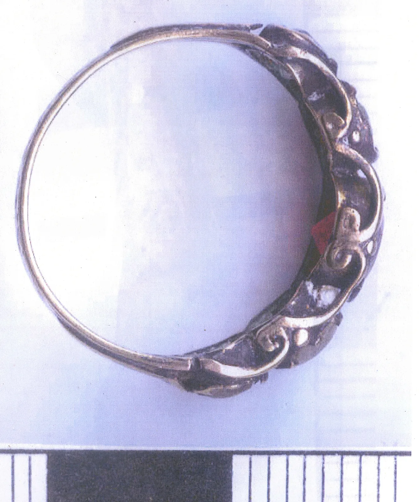 Victorian gold band photographed against a pale ground with a scale bar, the outer surface chased with a scrolling pattern