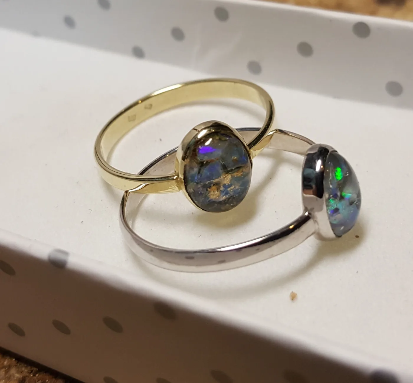 Two opal rings side by side on a white box, one in yellow 585 gold and one in 925 silver, each set with an oval Slovak opal