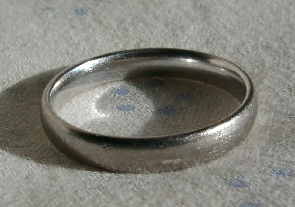 Plain white gold band lying on a white surface, the rhodium plated surface reflecting light unevenly around the shank