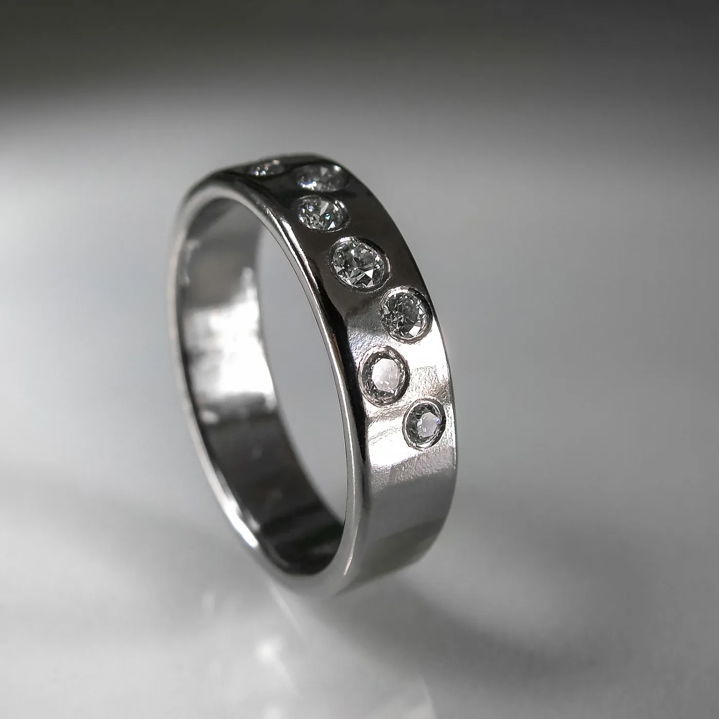 Wide white gold band set flush with a scattering of small diamonds across its polished surface