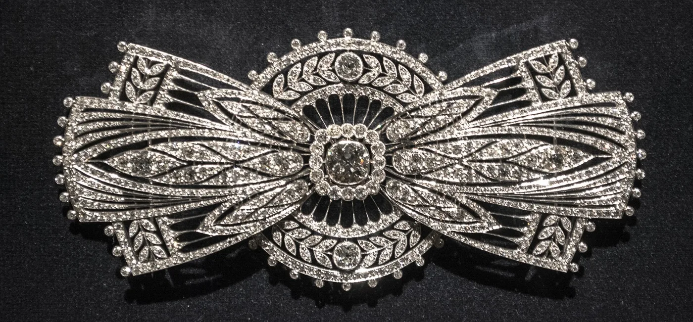 Wide bow-shaped brooch in white metal, densely set with diamonds across looping ribbon forms
