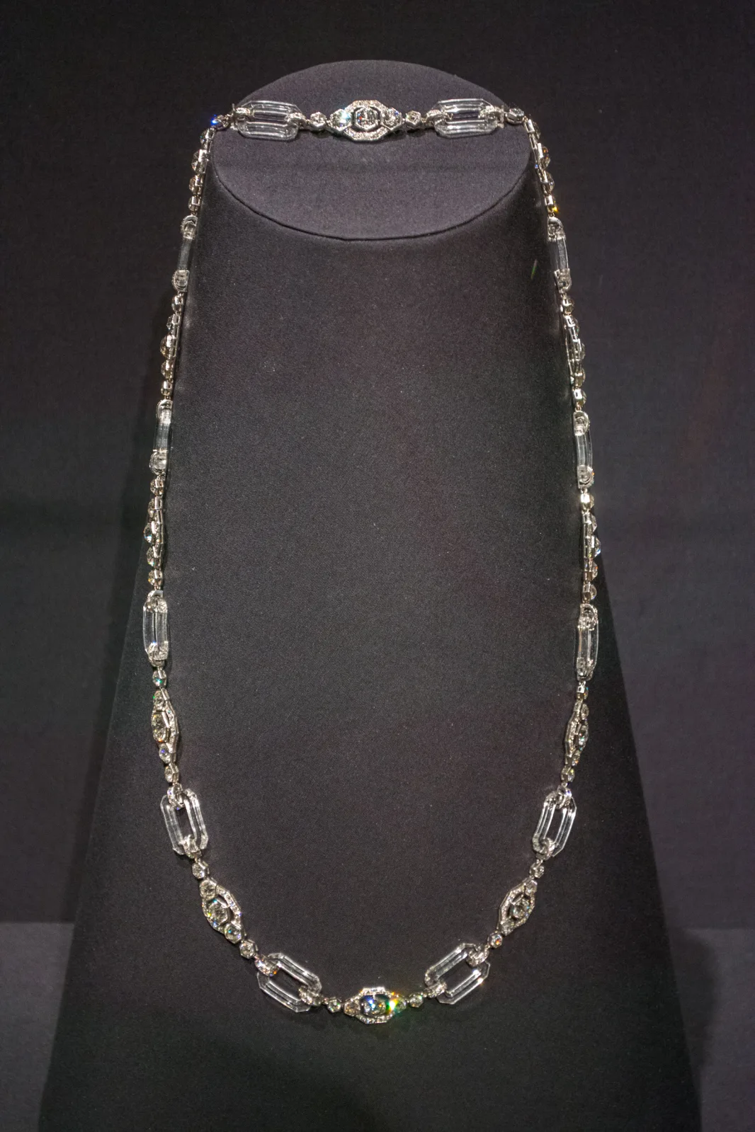 Long diamond sautoir necklace in white metal, hanging in a single line against a dark background