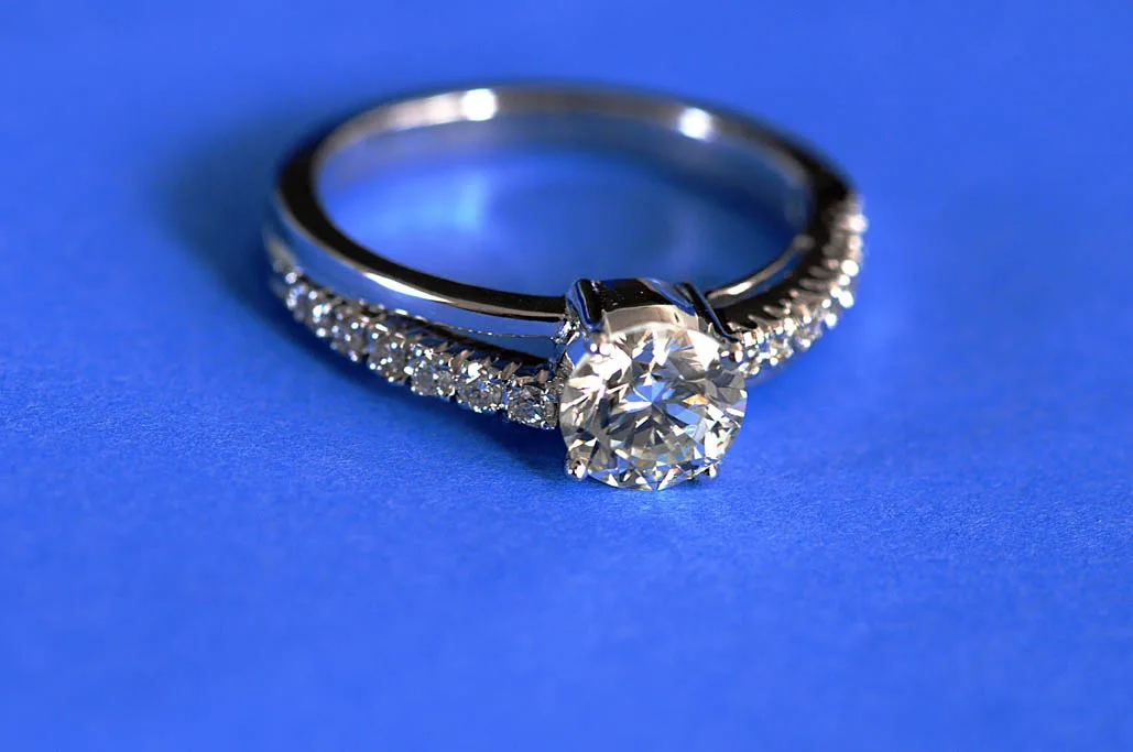 White metal solitaire ring with a raised claw setting, photographed against a plain blue ground