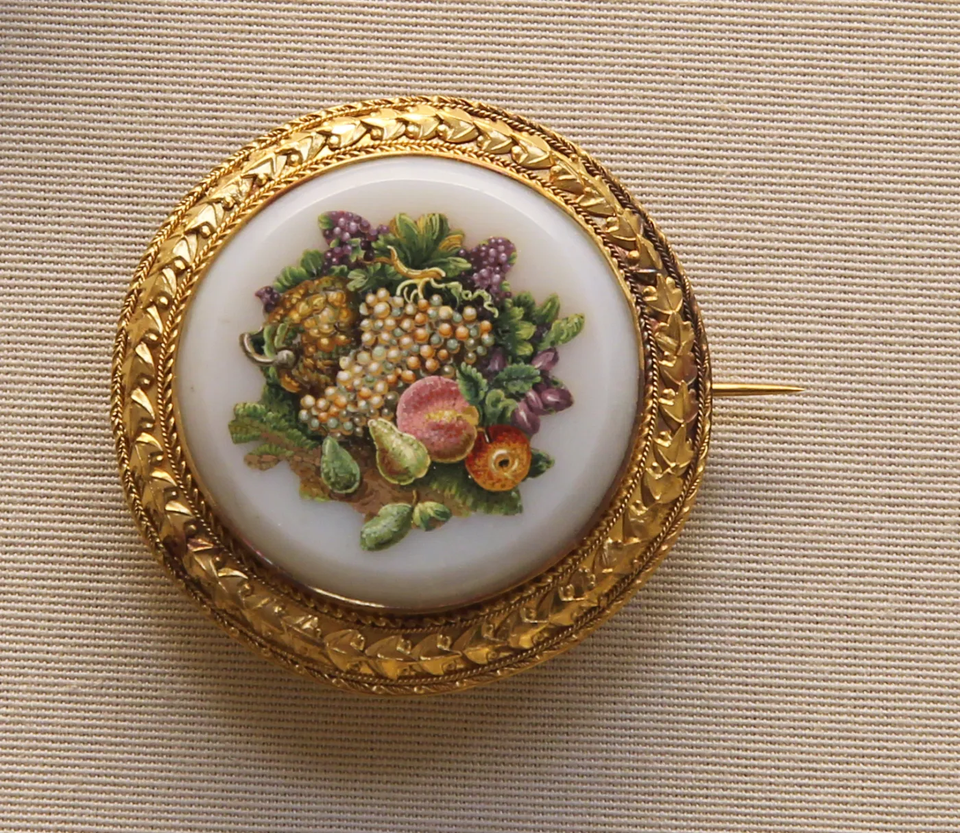 Round gold brooch with a chased laurel border, its centre a micromosaic of grapes, a pear, a strawberry and foliage set into a white opaline glass field