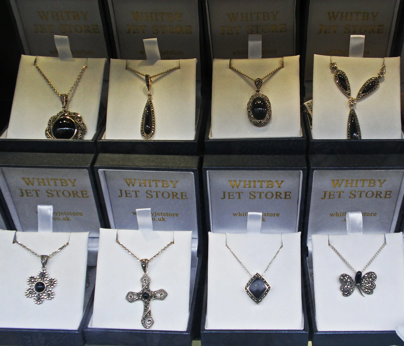 Carved Whitby jet pendants and necklaces displayed on cards, including a cross, a butterfly and faceted teardrop drops in matte black