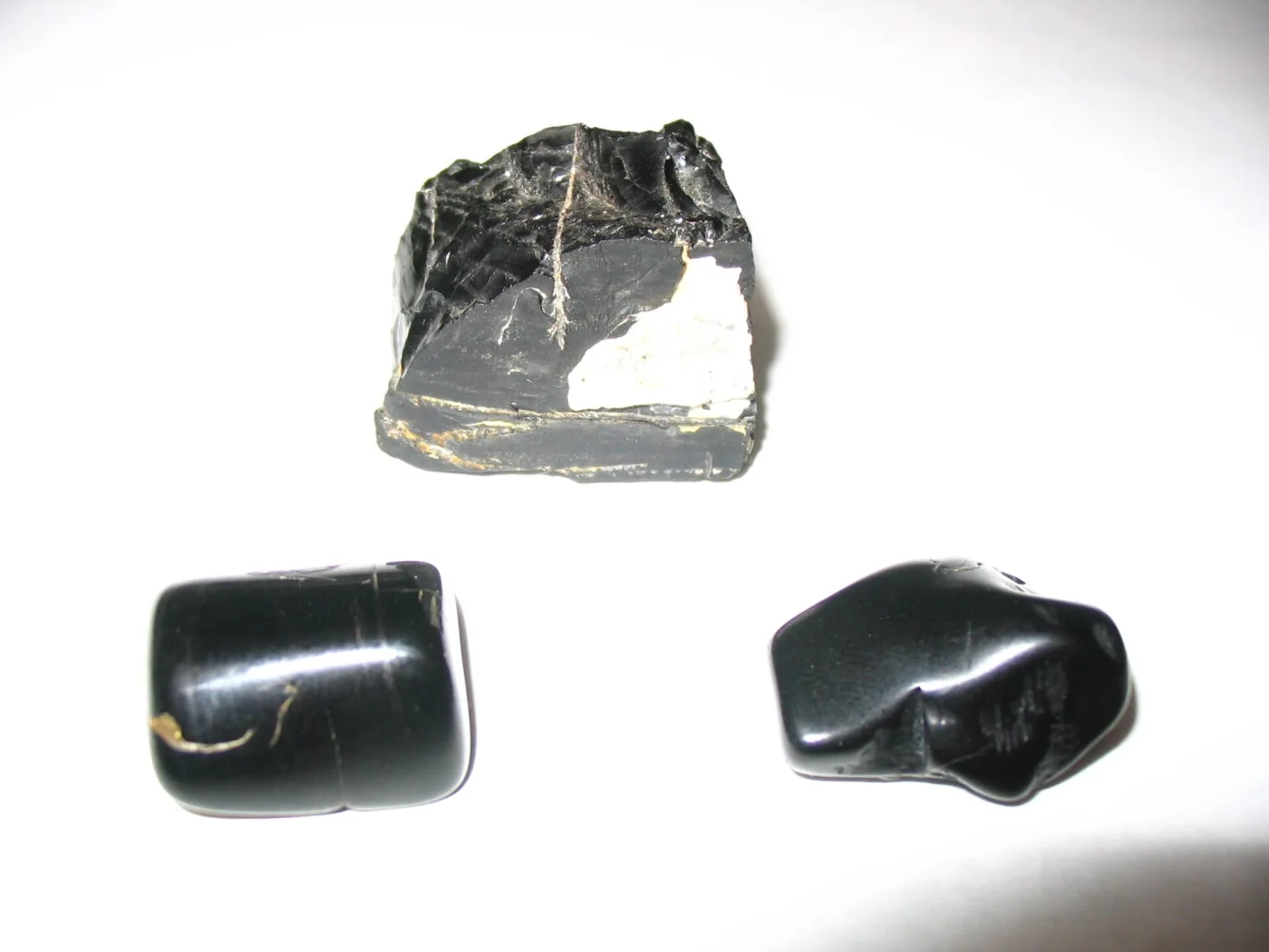 A rough lump of natural jet beside two polished pieces, the polished faces showing a soft resinous sheen against the dull matte fracture of the raw stone