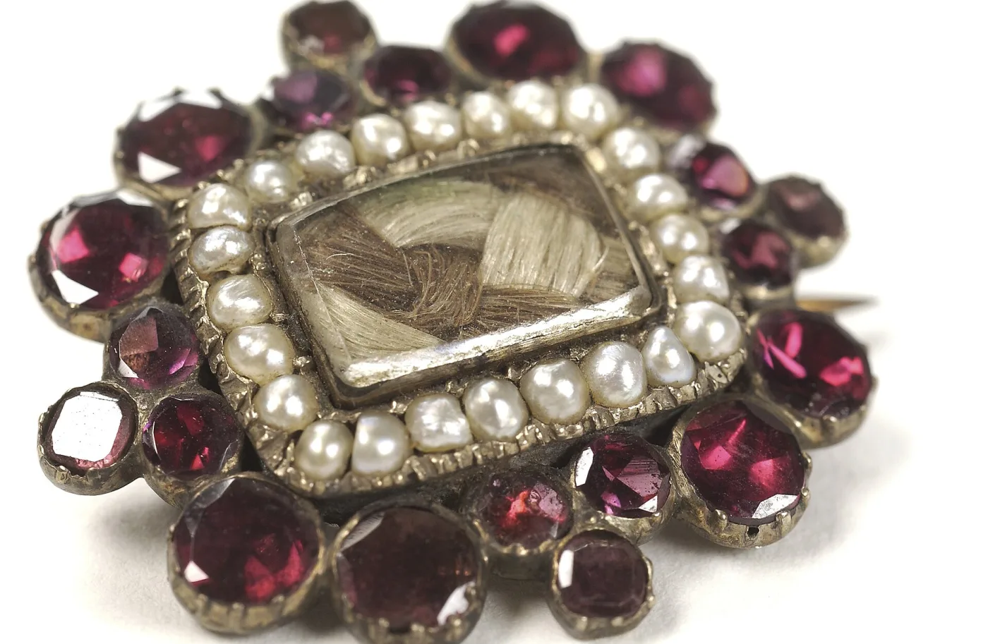 Mourning brooch holding a panel of woven hair beneath glass, framed by an outer border of garnets alternating with seed pearls