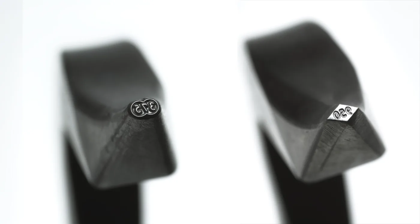 Two steel hallmarking punches seen end-on: the left strikes 375 inside an oval, the right strikes 950 inside a diamond-shaped frame, both cut in reverse