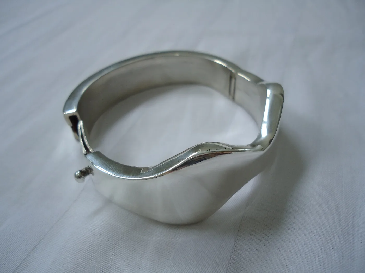A wide polished silver cuff bracelet with a hinged clasp, photographed on a white background